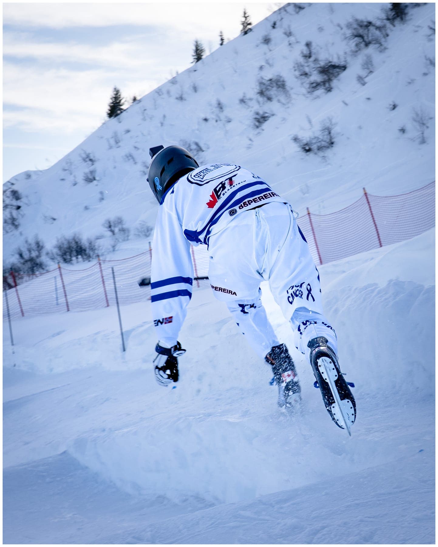 A rider in a white race suit crouched into a turn, seen from behind