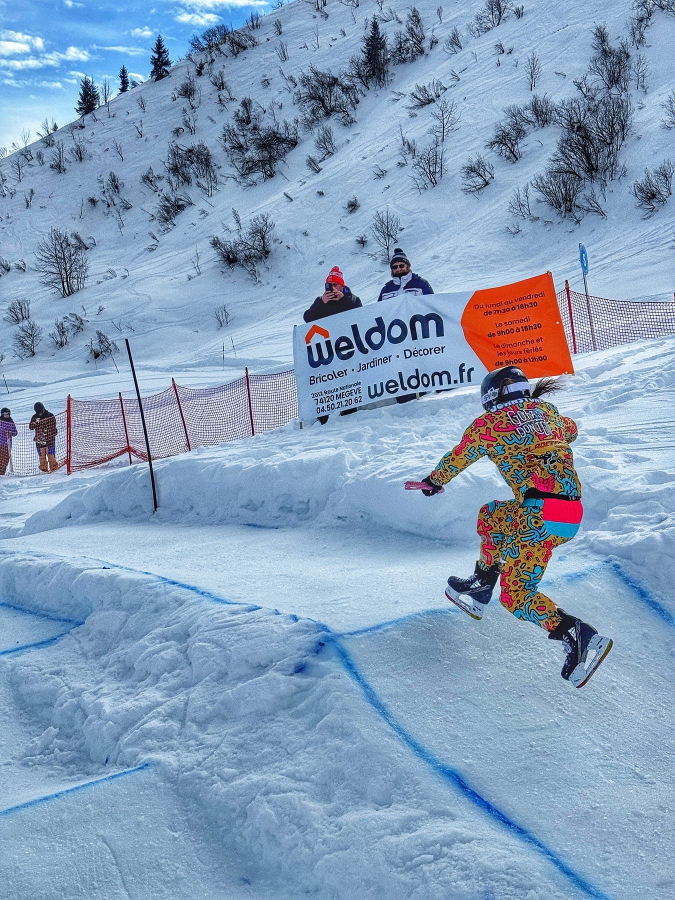 A rider in a colourful patterned suit skating past a sponsor banner