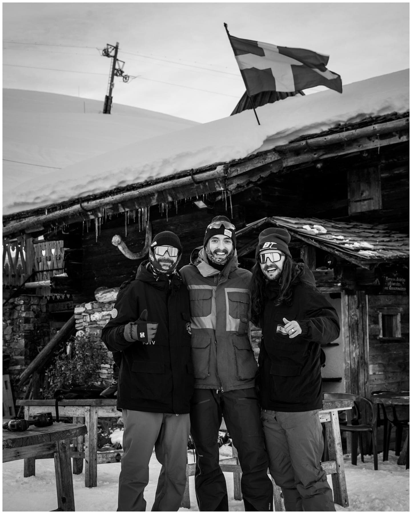 Three members of the crew in front of a chalet flying the Savoie flag