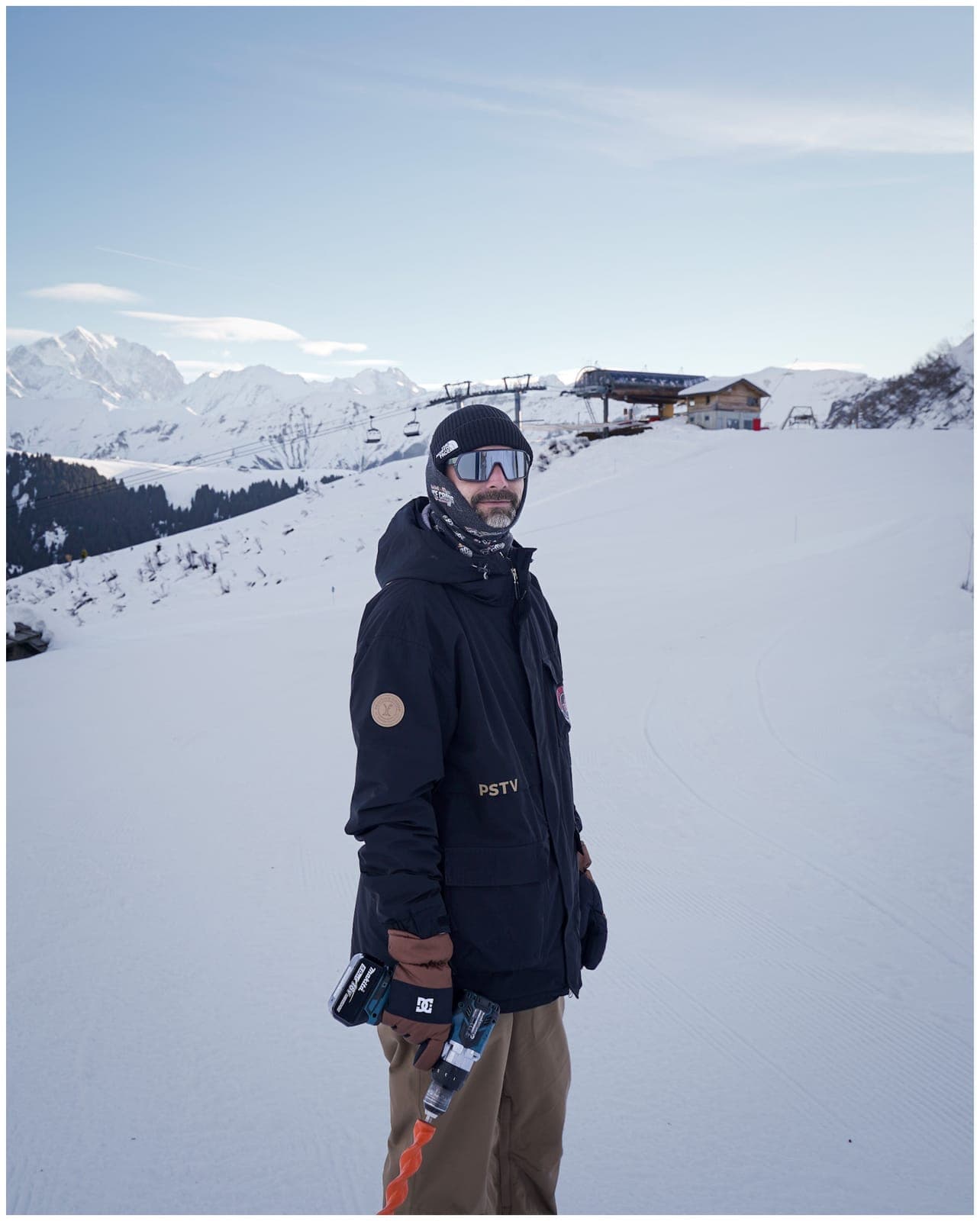 A crew member standing on the snowy slope, a drill in hand