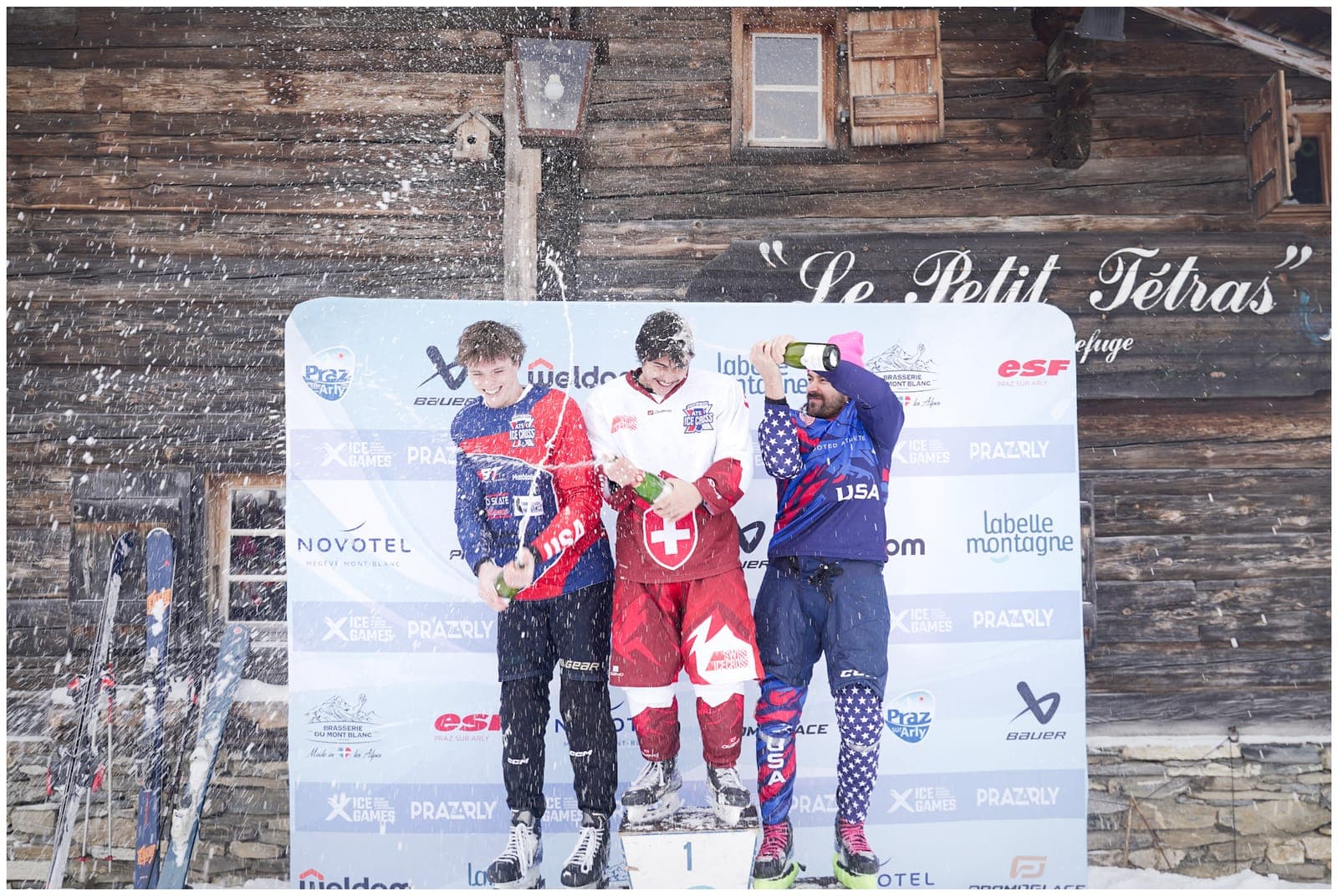 Three riders celebrating on the race-day podium, spraying champagne