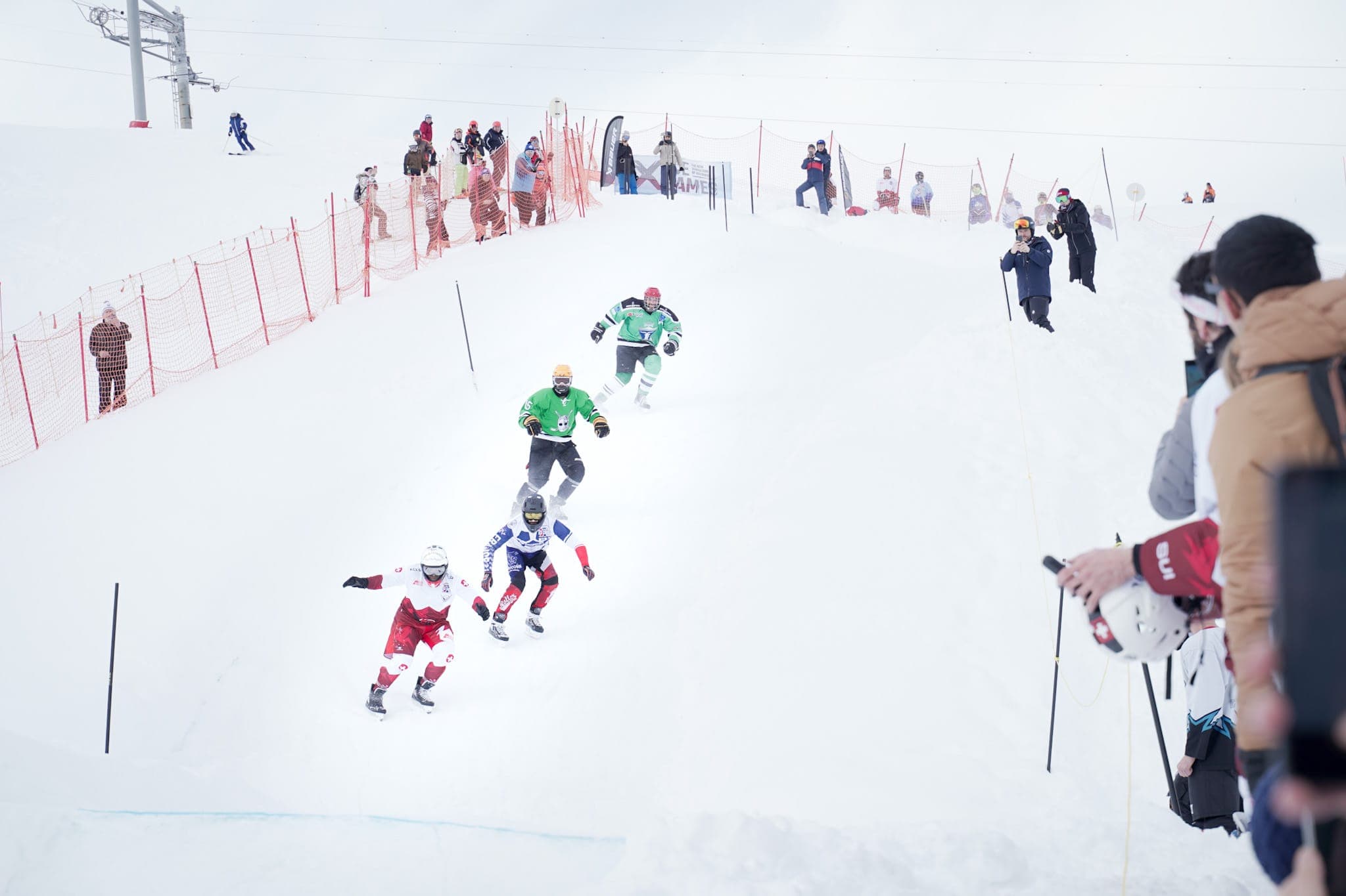 Riders descending the track in single file, watched by spectators along the fence